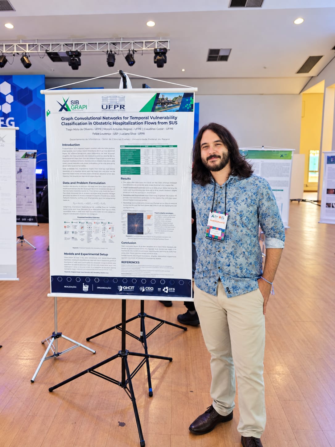 Author standing beside the printed poster during the SIBGRAPI 2026 poster session