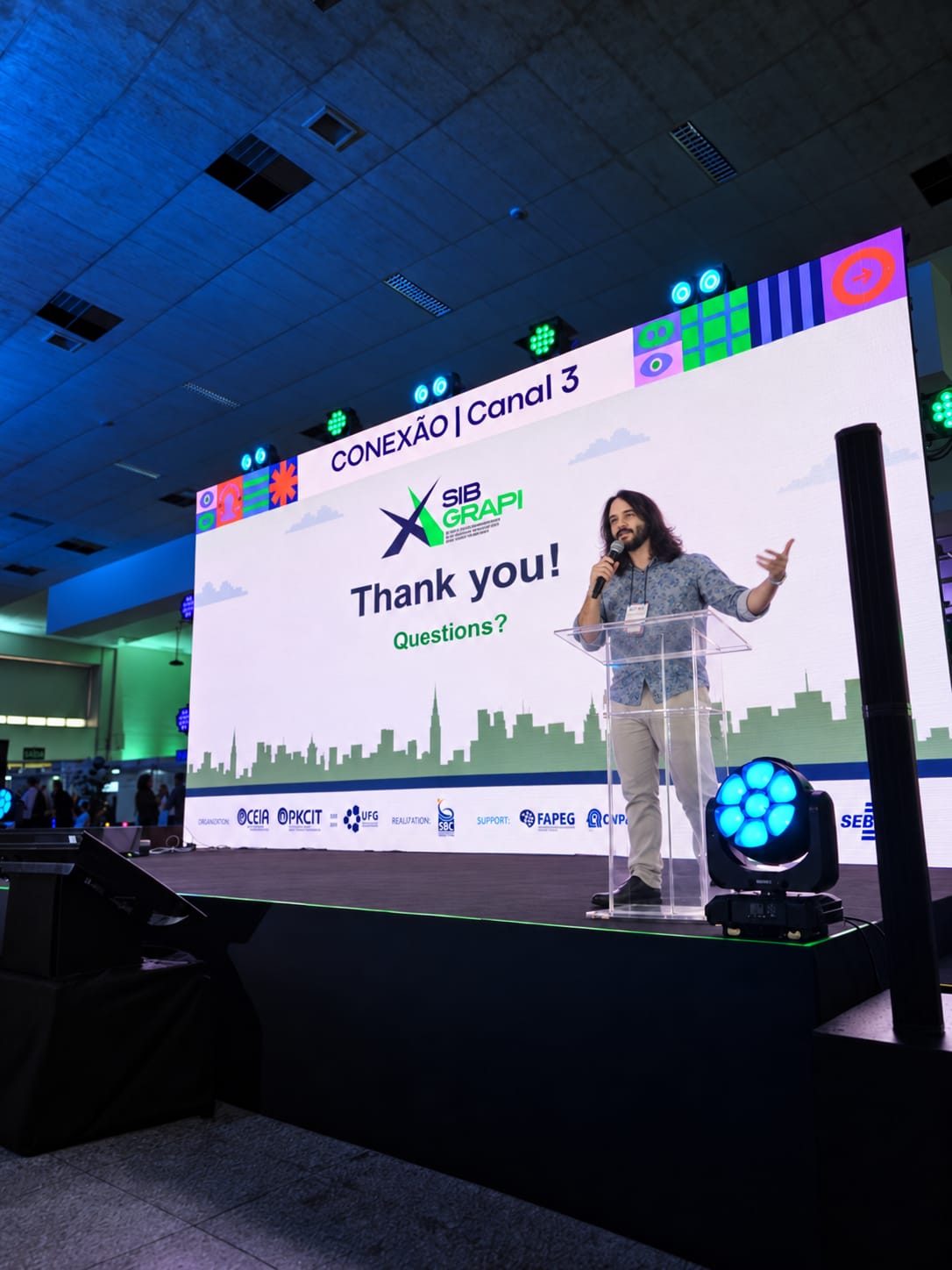Author presenting on stage at SIBGRAPI 2026, with the closing slide projected behind